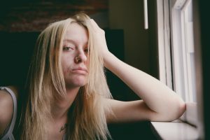 Mujer apoyada en una ventana sosteniendo su cabeza con el brazo, con mala cara y posibles síntomas de estrés. como combatir la ansiedad, nervio vago, técnicas de relajación, combatir la depresión. 